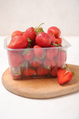 Hafif arka planda taze çilekli plastik konteynır, yakın plan.