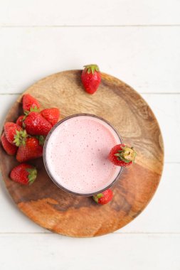 Hafif ahşap arka planda bir bardak lezzetli çilekli smoothie.