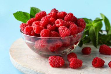 Mavi arka planda taze ahududu ve nane şekerli cam kase.