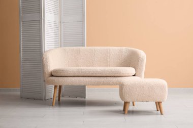 Bej duvarın yanında beyaz kanepe ve katlanır ekran.