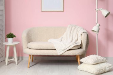 Sıcak beyaz kanepe, yastıklar ve pembe duvarın yanındaki lamba.