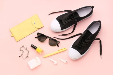 Şık güneş gözlüklü kompozisyon, modern kulaklıklar, spor ayakkabılar ve pembe arka planda oje.