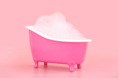 Pembe arka planda tüylü sabun köpüğü olan küçük bir küvet.