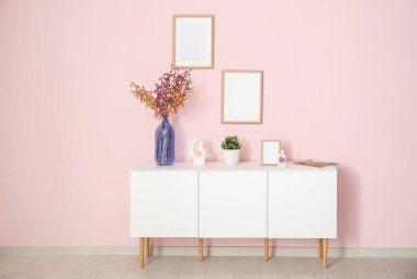 Dekorlu beyaz büfe ve pembe duvarın yanında boş çerçeveler.