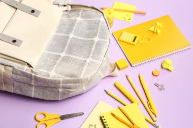 Leylak arka planında farklı kırtasiye malzemesi olan şık bir okul çantası.