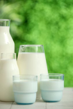 Bardaklar ve şişeler beyaz fayans masasında taze süt.
