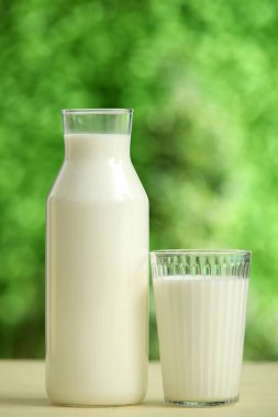 Dışarıdaki sarı ahşap masada bardak ve bir şişe taze süt.