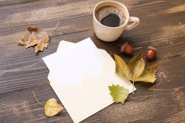 İçi boş bir kart, bir fincan aromatik kahve ve kahverengi ahşap arka planda sonbahar yaprakları.