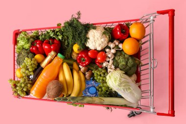 Pembe arka planda yiyecek dolu alışveriş arabası.