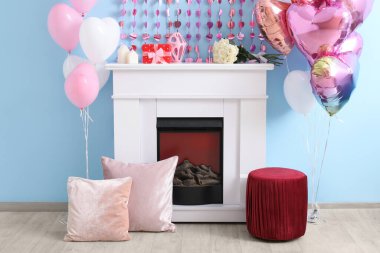 Mavi duvarın yanında kalp şeklinde balonları ve çelenkleri olan bir şömine. Sevgililer Günü kutlaması