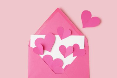 Renkli arka planda kart ve kağıt kalpler olan pembe bir zarf. Sevgililer Günü kutlaması