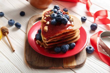Kalp şeklinde leziz gözlemeler, hafif ahşap arka planda yaban mersini ve reçel, yakın plan. Sevgililer Günü kutlaması