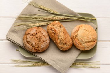 Lezzetli çörekleri ve beyaz ahşap arka planda buğday kulakları olan tabaklar.