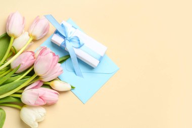 Sarı arka planda hediye kutusu ve zarfı olan bir buket güzel lale. Uluslararası Kadınlar Günü