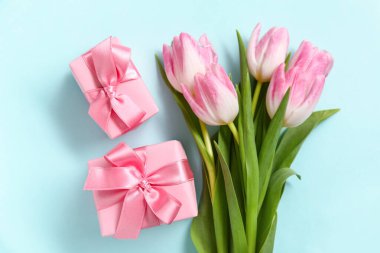 Mavi arka planda hediye kutuları olan pembe laleler.
