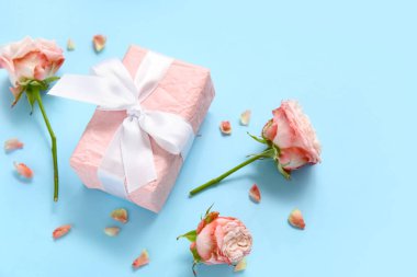 Mavi arka planda güller ve taç yaprakları olan hediye kutusu