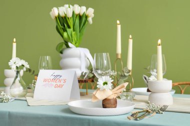 Yeşil duvarın yanındaki Uluslararası Kadınlar Günü kutlamaları için yanan mumlar ve lale çiçekleriyle güzel bir masa.