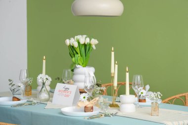 Yeşil duvarın yanındaki Uluslararası Kadınlar Günü kutlamaları için yanan mumlar ve lale çiçekleriyle güzel bir masa.