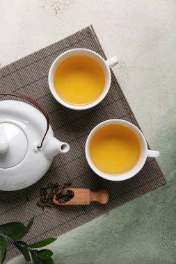 Çaydanlıklı bambu hasırı, bir fincan çay ve yeşil grunge arka planda yapraklar.