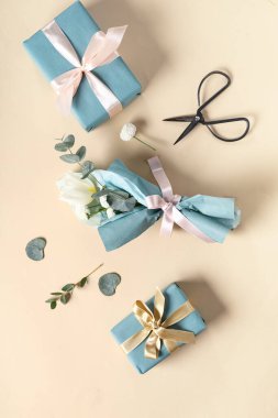 Okaliptüs, makas ve bej arka planda hediye kutularıyla ambalaj kağıdına sarılmış küçük bir buket güzel bahar çiçeği. Uluslararası Kadınlar Günü