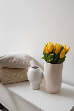 Işık duvarının yanındaki tuvalette lale ve yastıklı vazolar.