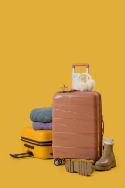 Sarı arka planda kalın elbiseli bavullar.