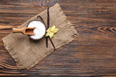 Bir kase vanilya tozu, sopalar ve çiçek ahşap arka planda.