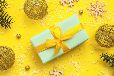 Noel hediyesi kutusu, köknar dalları, toplar ve sarı arka planda tahta kar taneleri.