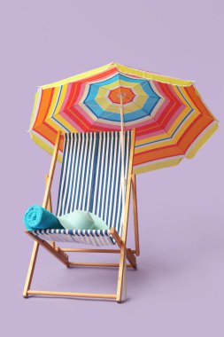 Renkli şemsiyeli çizgili iskemle, eflatun arka planda şapka ve havlu.