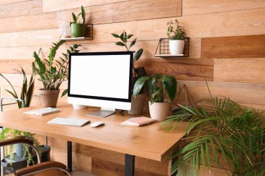 Ofisteki ahşap duvarın yanında boş bilgisayar monitörlü ve yeşil çiçekli bir işyeri.
