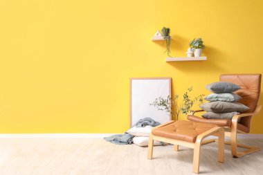 Sarı duvarın yanında kahverengi koltuklar ve yumuşak yastıklar.