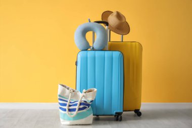 Sarı duvarın yanında boyun yastığı, şapka ve plaj çantası olan bavullar.