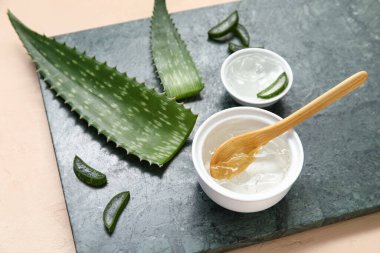Bej arka planda yaprakları olan bir kase aloe vera jel ve pano.