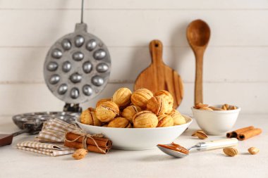 Lezzetli ceviz şekilli kurabiyeler, tarçın, badem ve ahşap masa üzerinde pişirme biçimi olan bir kase.