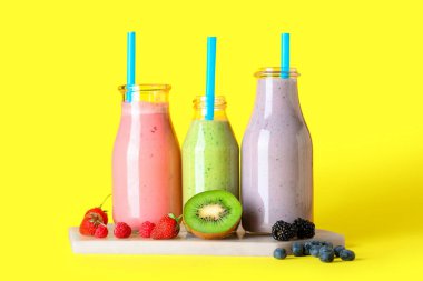 Sarı arka planda farklı böğürtlenli taze meyve suyu şişeleri.
