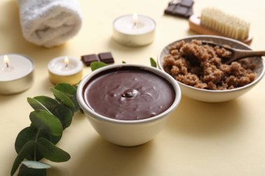 Soluk sarı arka planda erimiş çikolata ve yeşil dallı spa kompozisyonu, yakın plan.