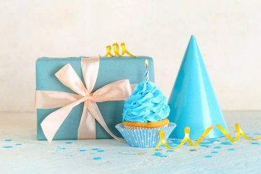 Tatlı doğum günü keki yanan mum, hediye kutusu ve açık mavi masada parti şapkası