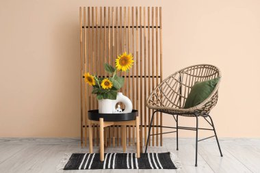 Sandalyesi, katlanır ekranı ve vazosu olan şık bir oda bej duvarın yanındaki sehpanın üzerinde ayçiçeği buketi.