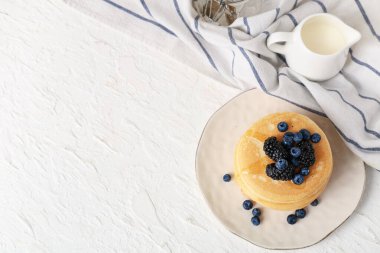 Beyaz arka planda taze yaban mersini, böğürtlen ve sütle kaplı bir tabak tatlı krep.