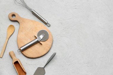 Paslanmaz çelik pizza kesicisi ve arka planda farklı mutfak aletleri olan kompozisyon.