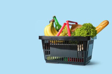 Farklı taze ürünlerle dolu siyah alışveriş sepeti ve mavi arka planda baget.