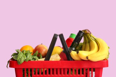 Farklı taze ürünlerle dolu kırmızı alışveriş sepeti ve leylak arka planda muzlar