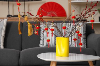 Ağaç dalları ve yeni yıl kutlamaları için Japon sembolleri olan vazo oturma odasındaki masada.
