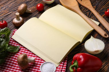 Siyah ahşap zemin üzerine boş tarif defteri, peçete ve malzeme içeren kompozisyon