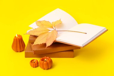 Kitap yığını, sonbahar yaprağı ve sarı arka planda yanan mumlar.