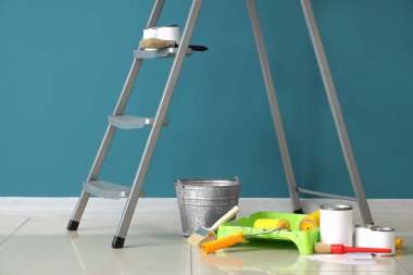 Mavi duvarın yanında boya ve aletlerle dolu bir merdiven.