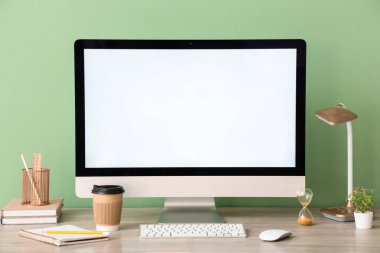 Modern bilgisayarlı şık bir iş yeri, bir fincan kahve, lamba ve ofis duvarının yanındaki kırtasiye malzemeleri.