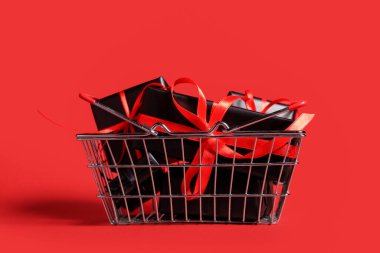 Kırmızı arka planda hediye kutuları olan alışveriş sepeti. Kara Cuma indirimi