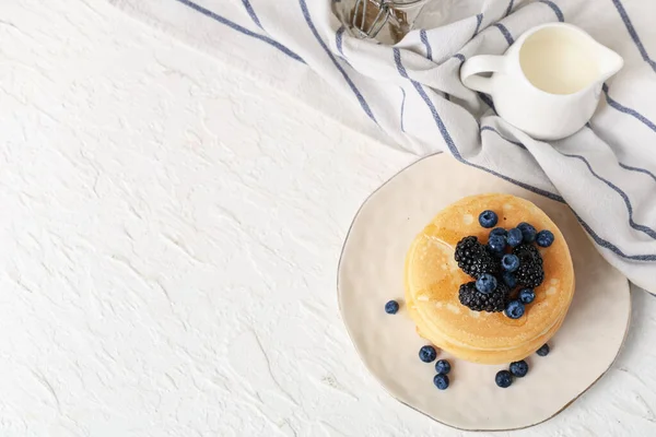 Beyaz arka planda taze yaban mersini, böğürtlen ve sütle kaplı bir tabak tatlı krep.