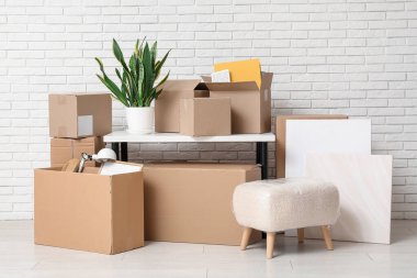 Beyaz tuğla duvarın yanında ev bitkisi ve karton kutularla dolu bir masa. Taşınma konsepti